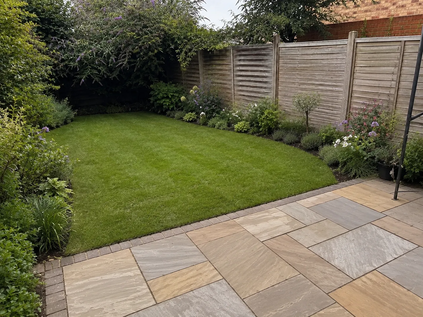 The same garden after Greenford's redesign — a new striped lawn, planted borders and a clean sandstone patio.