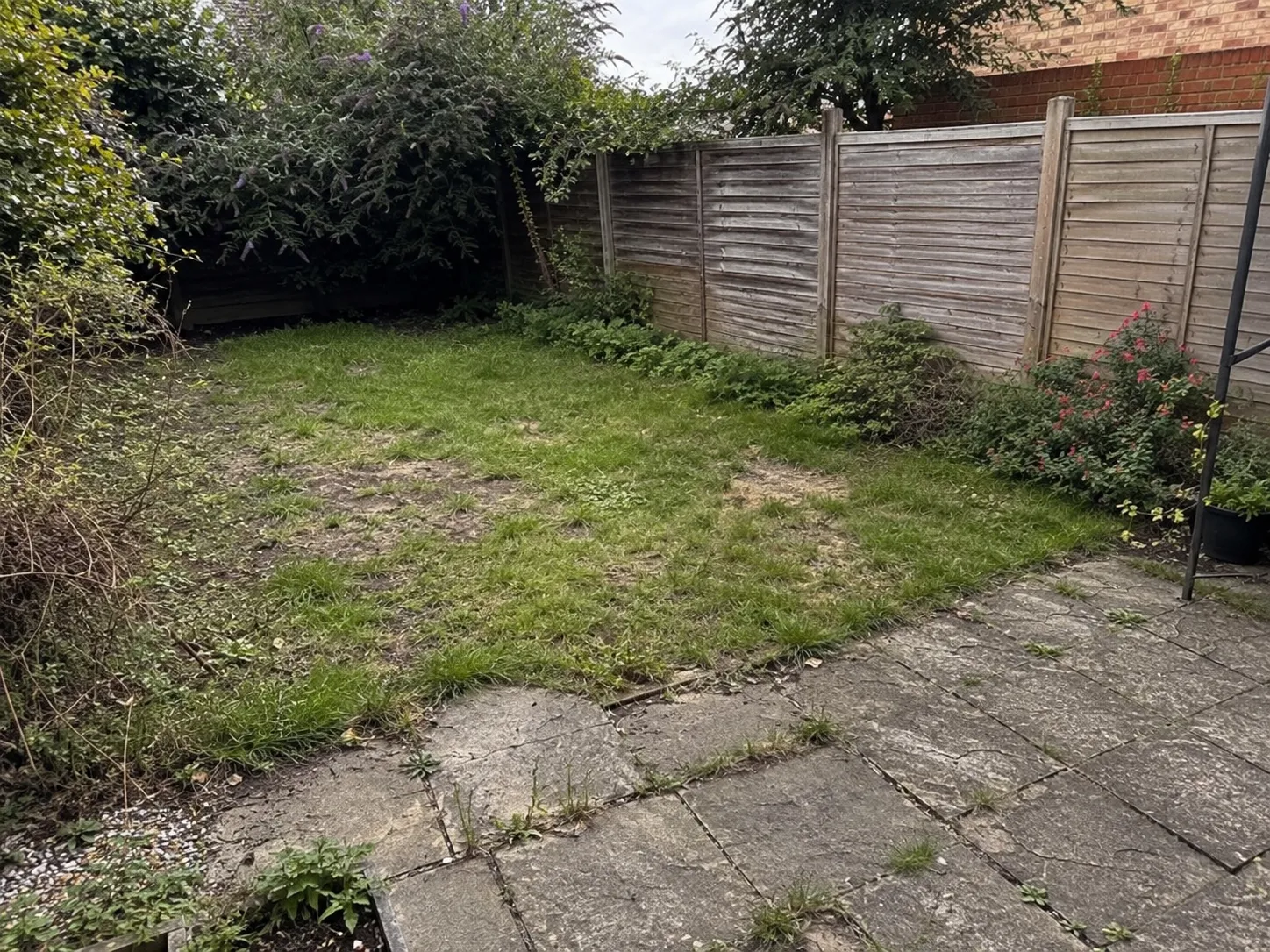 A tired Cardiff back garden before Greenford's work — patchy lawn and mossy, cracked paving.